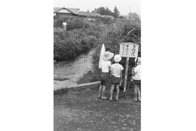 写真：川の傍で「きけん」の立て札を見ている子供たち